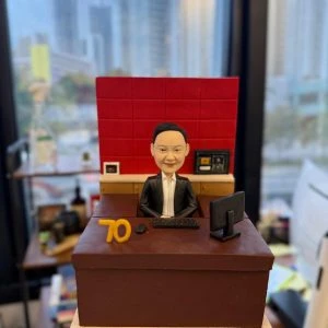 專為老闆與資深領袖打造的人像公仔，以辦公室實景為靈感：深棕色主管書桌、紅色背板、電腦螢幕與鍵鼠、文件抽屜等細節完整重現，並加入「70」里程碑數字象徵榮耀與成就。質感造型結合專業氛圍，適合作為高層榮休禮物、周年紀念或團隊致敬贈禮；可全方位客製服裝、桌面配件、祝福銘牌與包裝，讓心意更具故事與收藏價值。Keywords：高層榮休禮物，人像公仔，老闆。