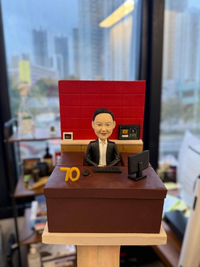 專為老闆與資深領袖打造的人像公仔，以辦公室實景為靈感：深棕色主管書桌、紅色背板、電腦螢幕與鍵鼠、文件抽屜等細節完整重現，並加入「70」里程碑數字象徵榮耀與成就。質感造型結合專業氛圍，適合作為高層榮休禮物、周年紀念或團隊致敬贈禮；可全方位客製服裝、桌面配件、祝福銘牌與包裝，讓心意更具故事與收藏價值。Keywords：高層榮休禮物，人像公仔，老闆。