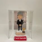 退休老師禮物人像公仔，灰白短髮，戴眼鏡，身穿黑色西裝配白色恤衫，雙手交疊站於淺色底座，底座刻有「Happy retirement to Siles」字樣，旁邊放置金色獎盃，收藏於透明展示盒內。