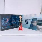 科技罪案與數位鑑識主題的人像公仔：短髮戴眼鏡的角色身著黑色西裝，手持平板坐在鮮紅色高腳凳上；背板左側為深藍數位網格與電路紋理設計，標示 Cyber Range 與 Cyber Security and Technology Crime Bureau 字樣；右側為淺灰藍色走廊與 Digital Forensics Complex 標誌，並見 Cyber Security and Technology Crime Bureau 的牆面標示。地面為白灰色細點質感，整體呈現與【鑑證科】、數位鑑識或科技罪案調查相關的警察單位氛圍，適合作為警務人員禮物或警察人像公仔的專業場景。