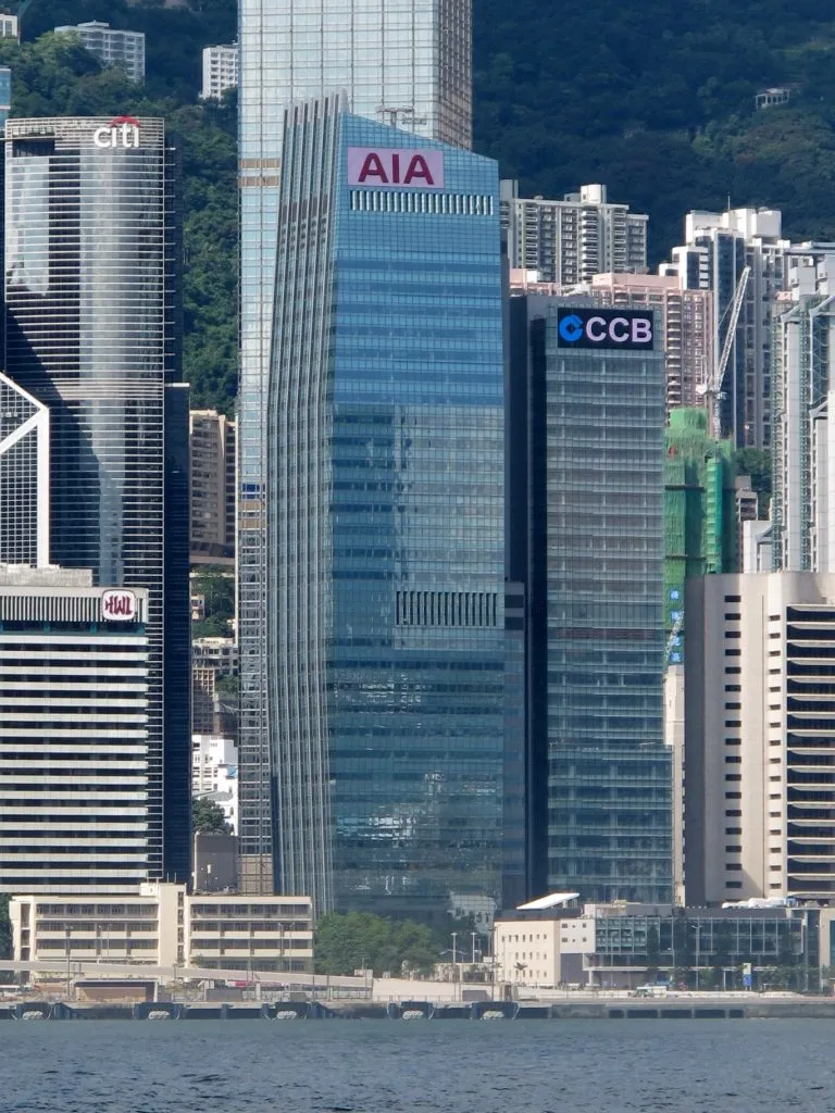 從維港遠眺友邦保險 (AIA) 總部大樓，玻璃幕牆反射著藍天，大樓頂部清晰可見 AIA 標誌，象徵輝煌成就，是贈送榮休禮物的理想地標。