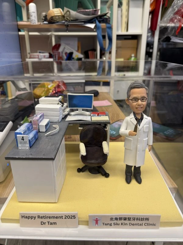 (客製化「牙醫博士榮休」診所場景紀念公仔 Q版牙醫公仔（身穿專業白色醫師袍、深色格紋襯衫與深色西裝褲，配戴金屬框眼鏡的資深男士，頭髮灰白梳理整齊，右手手持牙科器械，面帶親切微笑，展現專業與慈祥的醫者風範） 微縮牙科診所場景（L型辦公桌上細節豐富，擺放有電腦螢幕、鍵盤、多層文件架/印表機，以及多盒藍色與紫色的牙科耗材包裝盒，桌角立有寫著「4」的標示牌；後方配置一張黑色皮革旋轉辦公椅；底座為暖黃色，前方設有兩個紀念牌，左側印有「Happy Retirement 2025 Dr Tam」，右側印有「北角鄧肇堅牙科診所 Tang Siu Kin Dental Clinic」及標誌） 牙醫權威、榮休紀念、專業職人、診所日常、資深醫師 榮休禮物、醫師紀念、診所擺飾、感謝師恩、職業生涯里程碑)