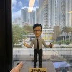 (客製化Q版人物公仔——專業男教師手持文具紀念擺飾 手工人物公仔細節（圖片展示了一尊客製化的Q版男性人物黏土公仔，主角戴著黑框眼鏡，身穿淺藍色長袖襯衫並打著深色領帶，下身搭配黑色西裝褲與皮鞋，展現專業俐落的形象。公仔雙手張開，右手持有一把長尺，左手拿著一台計算機，暗示其可能為數學或理科教師。公仔站立於一個仿水泥質感的灰色方形底座上，底座前方貼有一塊金色名牌，黑字寫著「萬能的譚Sir 『羅中』同事致敬」，表達了同事間的敬意與讚賞） 環境背景與光影（公仔被一隻手托舉在空中，背景是一扇大落地窗。透過窗戶可以看到戶外清晰的城市景觀，包括高聳的白色住宅大樓、藍天白雲以及下方的街道與綠樹。室內天花板的長條形燈光倒映在玻璃窗上。自然光線從窗外透入，使公仔的輪廓清晰，面部表情溫和自然，背景的城市景觀為公仔提供了現代感的襯托） 軟陶公仔、真人公仔訂製、Q版人像、數學老師禮物、理科老師、教師節禮物、手工捏塑、客製化名牌、職業公仔、手持文具 同事送禮、榮休紀念、感謝師恩、辦公室擺設、獨家訂製紀念品、校園紀念、活動贈禮)