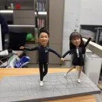 一對穿運動風服飾的情侶人像公仔在灰色幾何紋路底座上牽手張開雙臂擺姿勢