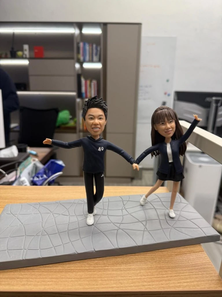 一對穿運動風服飾的情侶人像公仔在灰色幾何紋路底座上牽手張開雙臂擺姿勢