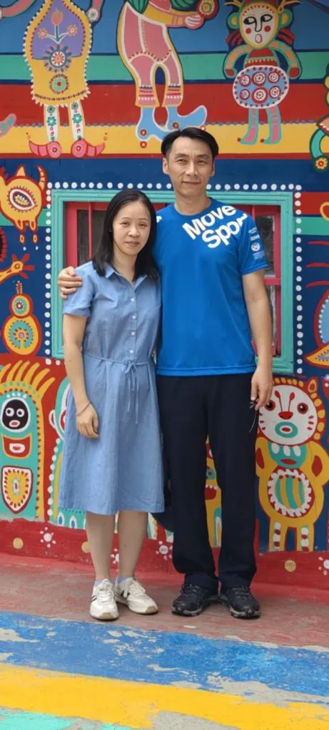一對情侶站在色彩繽紛的壁畫前合照，男士穿藍色T恤，女士穿藍色連身裙，展現了客製化公仔能捕捉的珍貴瞬間和永恆場景。
