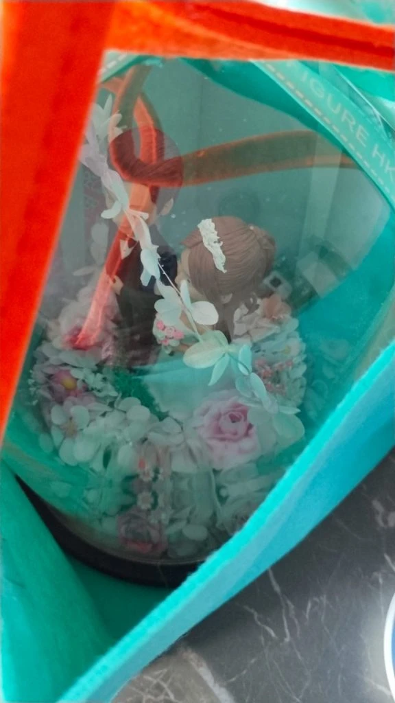 一對新人Q版真人公仔穿著婚紗禮服，在花束裝飾的玻璃罩內，將里程碑封存為永恆場景，是送禮首選的訂造人像公仔。