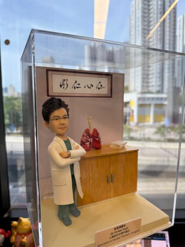 心胸肺外科醫生主題人像公仔穿白色醫師袍與手術服，雙手抱胸站在診間場景，旁有肺部模型與仁心仁術匾額，醫師開業與升遷客製禮