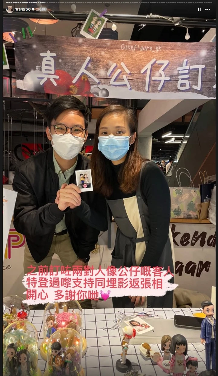 兩位戴口罩的顧客手持一張印有Q版真人公仔的拍立得照片，身後是寫有「真人公仔訂」的攤位背景，展現顧客對CUTEFIGUREHK的信賴。