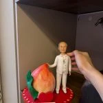 穿白色服飾的長輩人像公仔站在心形紅色底座上，旁邊放著巨型壽桃與祝壽刻字牌