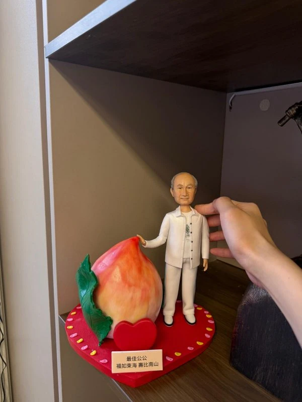 穿白色服飾的長輩人像公仔站在心形紅色底座上，旁邊放著巨型壽桃與祝壽刻字牌