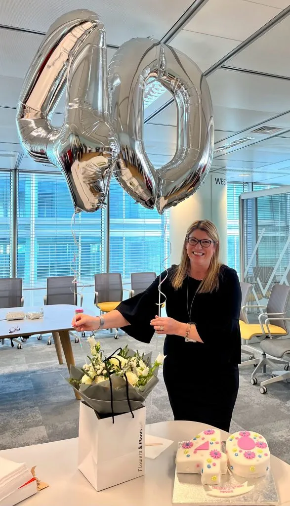 一位女性手持銀色「40」數字氣球，身旁有花束和生日蛋糕，慶祝香港職業生涯的里程碑，適合榮休或紀念禮物。