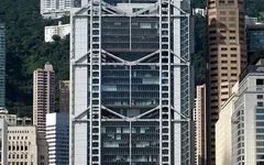 香港中環匯豐總行大廈的標誌性建築外觀，周圍環繞著其他高樓大廈，背景可見翠綠山坡。