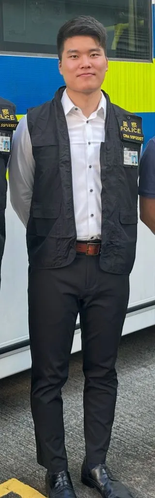 一位身穿白色恤衫、黑色背心和黑色長褲的紀律部隊人員，胸前掛有證件，展現專業氣場，是訂造人像公仔的靈感來源。