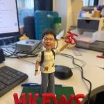 戴眼鏡的人像公仔背著背包、穿白色塗鴉T與灰色長褲，右手高舉紅色「35」，站在綠色草地底座，前方立體紅字「HKFWS」