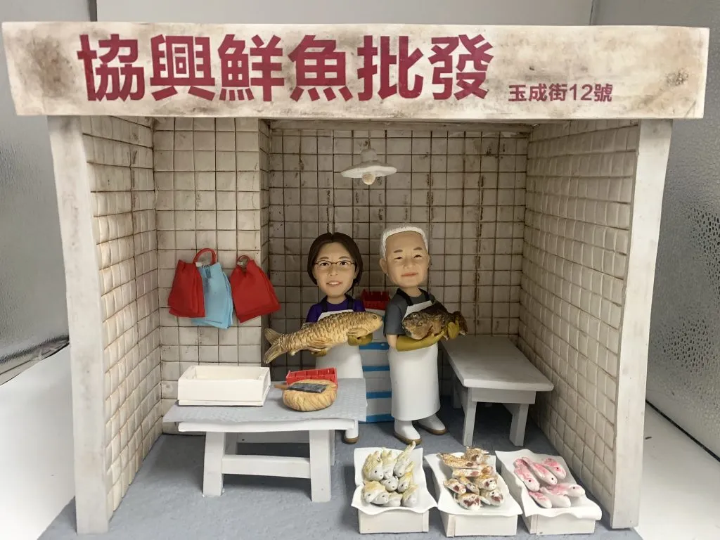 一對Q版真人公仔身穿圍裙，手持魚獲，站於迷你魚檔前，重現Modi Hair老闆的創業夢想，是獨一無二的訂造人像公仔禮物。