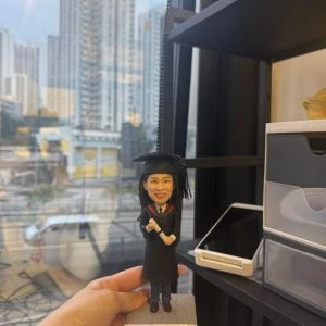 CUTEFIGUREHK 客製化女性人像畢業公仔,身穿黑色畢業袍並戴上四方帽,手持畢業證書,站在印有「Happy Graduation Anna 2026」專屬字句的石紋底座上,是送給大學畢業生的獨一無二紀念禮物。