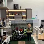 CUTEFIGUREHK 客製化香港交通警公仔。公仔身穿螢光黃綠色交通警制服，雙手交叉抱胸。旁邊配有一架精緻的警察電單車模型。場景背景為「上水警署」(Sheung Shui Police Station)。底座名牌刻有「退休不褪色 順樂永無憂 2026」，是一份專為警察訂製的榮休紀念禮物，裝在透明亞加力展示盒中。
