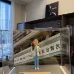 CUTEFIGUREHK 客製化女性醫生人像公仔，身穿藍色手術服和白袍並掛有聽診器。公仔放置於透明展示盒內，背景為律敦治醫院照片，底座設有刻上「仁心仁術」等真摯感謝字句的專屬牌匾，是病人送給醫生的獨一無二答謝禮物。