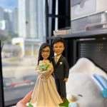 CUTEFIGUREHK 客製化夫妻結婚紀念人像公仔。女主角身穿白色婚紗、配戴眼鏡並手持淺藍色花球；男主角身穿深色西裝打領帶。綠色底座上的名牌刻有「Happy China Wedding Anniversary」的祝福語。這是一份專為慶祝結婚週年紀念度身訂造的浪漫禮物。