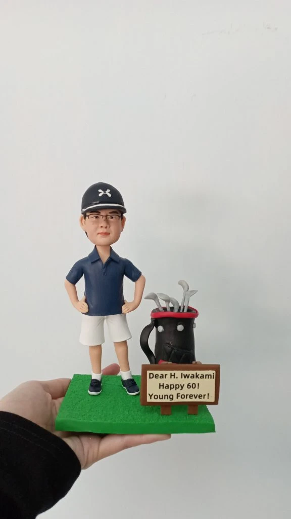 一個手持定制人像公仔的模型，人物穿著高爾夫球服裝，配戴棒球帽和眼鏡，站在綠色草地造型的底座上，旁邊有一個高爾夫球袋。