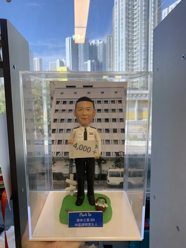 一款為香港警務人員訂製的退休人像公仔，主角為一名警官，身穿白色督察級制服，背景為中區警署，由其下屬為祝賀其2025年光榮退休而敬贈。