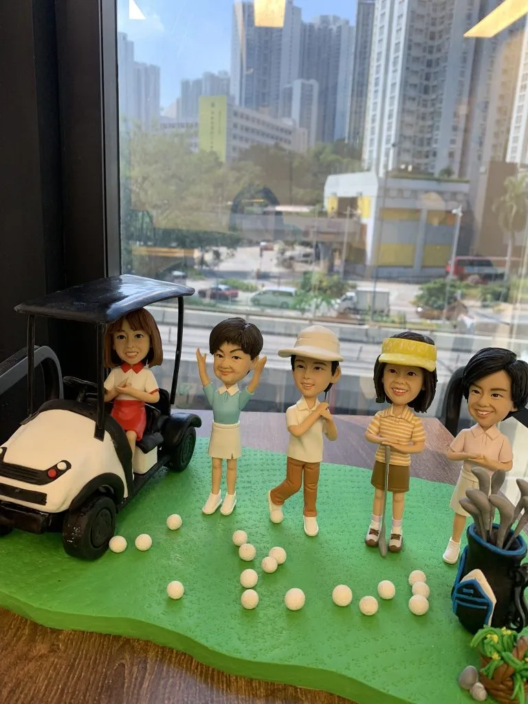 高爾夫主題人像公仔，一組五位人物公仔擺設，包含坐在球車上的女性、舉手歡呼的球手、手持球桿的男女，以及站立於球袋旁的公仔。場景佈置有綠色草地、球車與多顆高爾夫球，展現打球氛圍。