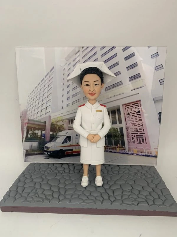 訂製醫護人像公仔，身穿白色護士制服與傳統護士帽，背景為醫院大樓與停泊的救護車，展示專業護士的典雅形象。這款公仔象徵醫生與醫護人員多年服務的感謝與榮耀，特別適合作為退休、升遷或致敬禮物。