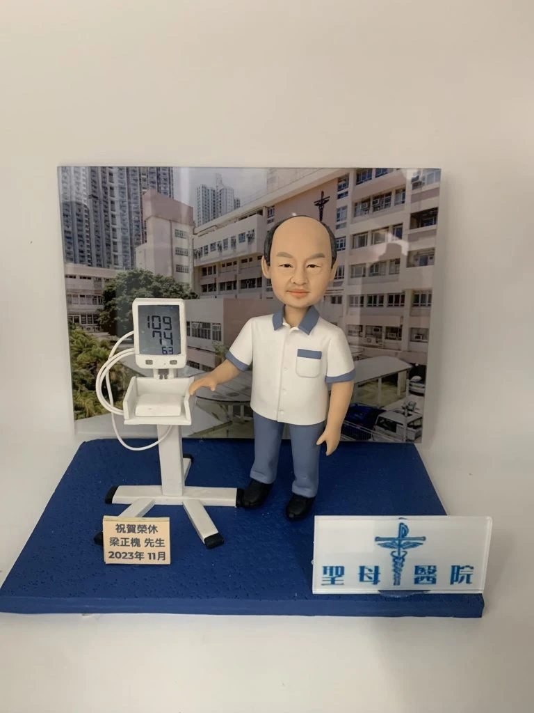 醫生人像公仔模型，身穿醫護制服，站立於醫院背景前方，手放在電子血壓計上，螢幕顯示血壓 109/74。此公仔為客製化醫護禮物，適合作為醫生退休紀念、醫護感謝或祝賀榮休的特別禮品。