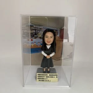 一款放置在透明亞加力膠盒中的客製化女士人像公仔，底座刻有聖經經文，背景為教室，是一份送給主日學老師或傳道人的感謝禮物。