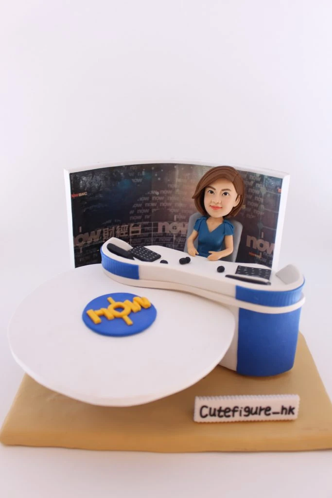 新聞演播室主題人像公仔：短髮女性報導員穿藍色上衣，坐在弧形主播台後方，桌面有麥克風與鍵盤；背板為新聞頻道演播室背景，前方白色圓台上有藍底黃字標誌；米色底座前擺有「Cutefigure_hk」名牌。整體專業而典雅，適合作為新聞部報導員退休禮物與榮退紀念擺設。