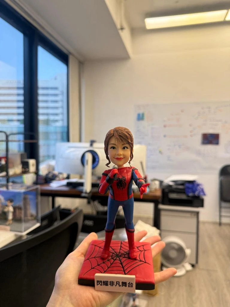 一款將女士頭像與蜘蛛俠身體結合的訂製人像公仔，她身穿蜘蛛俠戰衣，手持咪高峰，站在一個刻有「閃耀非凡舞台」字樣的紅色蜘蛛網地台上。