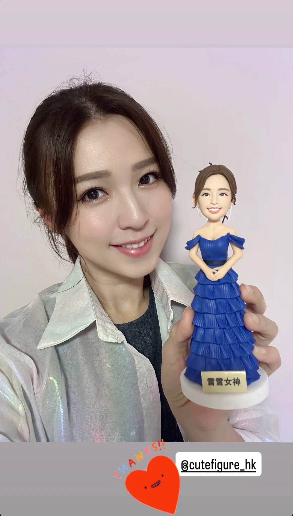 女子手持一個藍色多層荷葉禮服的人像公仔，公仔底座前牌寫有「雪雪女神」字樣；畫面右下角有「THANKS!!」與帳號貼圖。