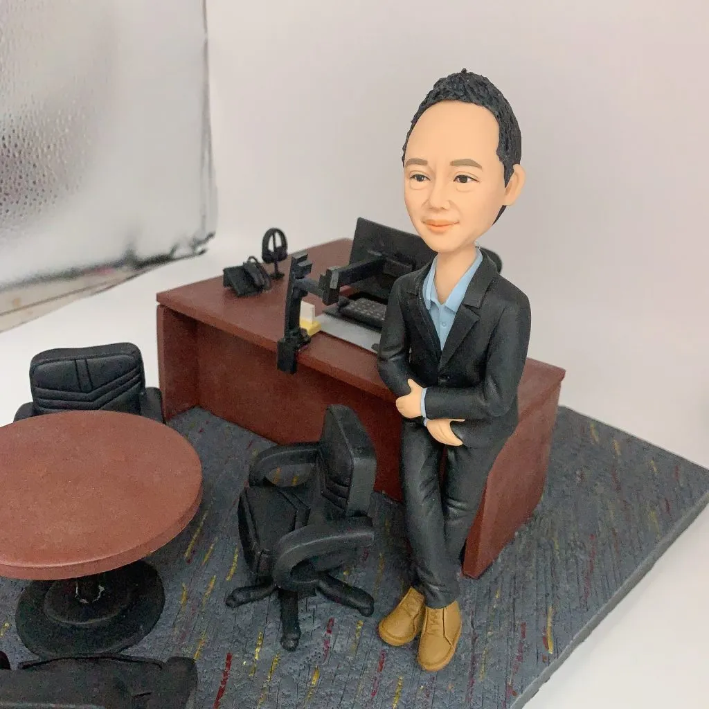 人像公仔辦公室場景:短髮男性公仔穿深色西裝外套與長褲、內搭淺藍襯衫,腳穿棕色皮靴,側身倚靠木質主管桌,雙手自然交疊。桌上配置筆電、螢幕支架、電話座與文具收納;一旁有黑色辦公椅與圓形會議桌,地面為帶有彩色線條的地毯紋理。整體呈現主管/經理級專業辦公氛圍的人像公仔擺設。