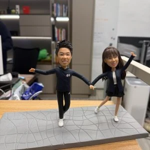 一對穿運動風服飾的情侶人像公仔在灰色幾何紋路底座上牽手張開雙臂擺姿勢