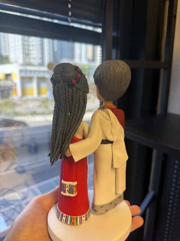 穿著民族傳統禮服的一對夫妻人像公仔站在白色圓形底座上，衣服圖騰與頭飾細節豐富