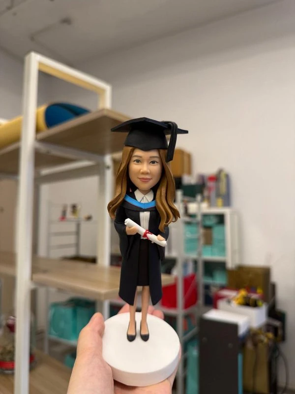 女畢業生公仔穿學士袍與方帽，手持文憑站在白色圓底座，畢業禮物可客製姓名與校色