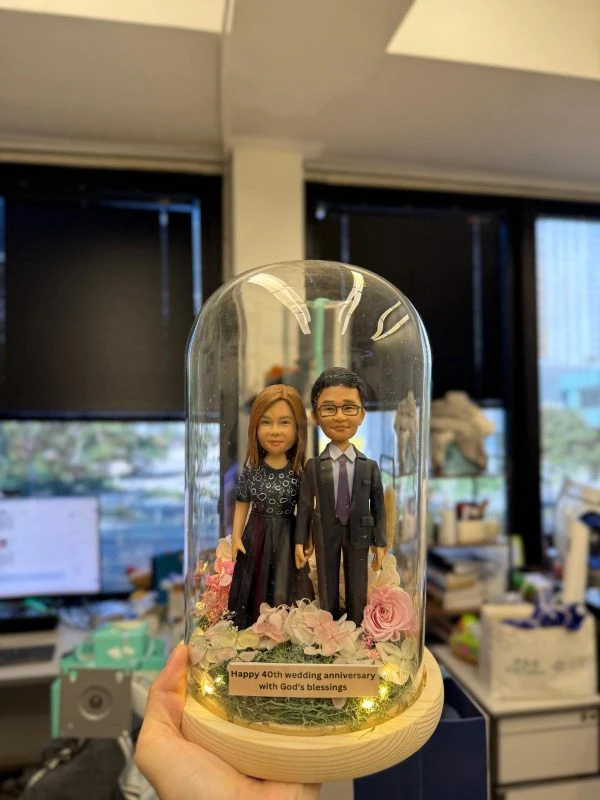 40 週年婚禮紀念雙人公仔以玻璃罩與木座呈現典雅儀式感，底部鋪滿粉色花材與暖燈，搭配客製金句銘牌。可自訂姓名、年份、服裝與祝福文字，亦能更換花色與燈光模式；精緻包裝、安全配送，讓相守不渝的愛被長久珍藏與展示。