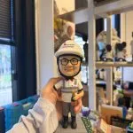 工程師主題人像公仔戴白色安全帽與對講耳機，穿公司POLO制服站在工地磚紋底座，手持香檳並配有姓名銘牌 Franklin Sare