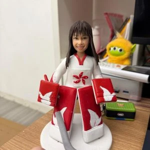 冰球門將主題公仔:長髮女孩穿白色球衣配紅色護具,胸前為五瓣花徽;雙手戴大面積護手、腿上穿紅白護腿,站在白色圓底座上微笑。