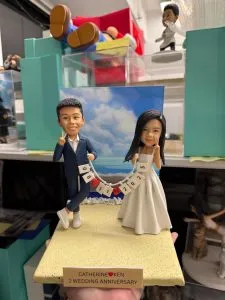 雙人婚禮公仔手拉日期旗串，沙灘背景與金色銘牌，結婚與週年紀念浪漫客製