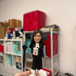 女律師主題人像公仔穿黑色法袍與白色領巾,手持法律判例手冊站在白色圓底座,律師節與執業授證客製禮