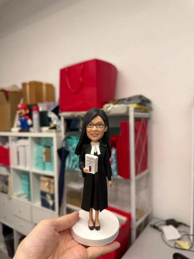 女律師主題人像公仔穿黑色法袍與白色領巾，手持法律判例手冊站在白色圓底座，律師節與執業授證客製禮