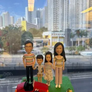 一家四口站在草地上的家庭人像公仔,旁邊有紅色跑車與野餐籃配件,呈現溫馨親子時光