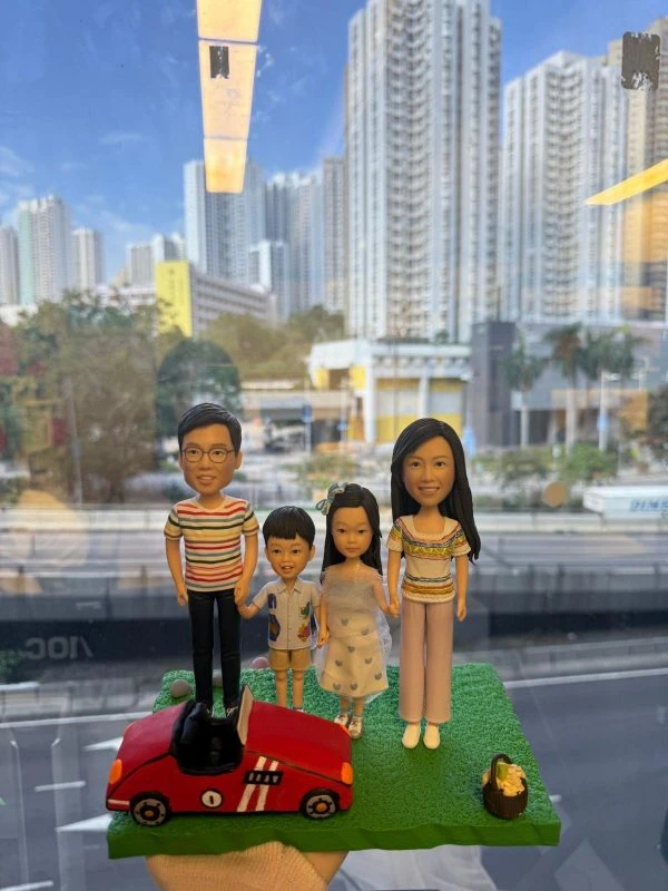 一家四口站在草地上的家庭人像公仔，旁邊有紅色跑車與野餐籃配件，呈現溫馨親子時光