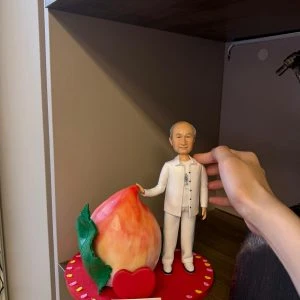 穿白色服飾的長輩人像公仔站在心形紅色底座上，旁邊放著巨型壽桃與祝壽刻字牌