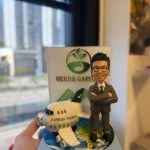 西裝人像公仔雙手交叉站在地球圖案底座旁，旁邊有印上 CATHAY PACIFIC 的小客機模型，後方立體背板寫有 SEEDS CAPITAL 與綠色標誌