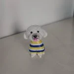 坐姿白色捲毛狗狗公仔，穿黃藍白條紋毛衣，黑鼻圓眼、粉紅舌頭微吐，放置在淺色桌面上。