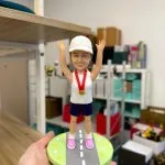 Alt: 女跑者公仔戴白帽掛金牌，雙手高舉站立於公路造型底座，馬拉松完賽紀念客製