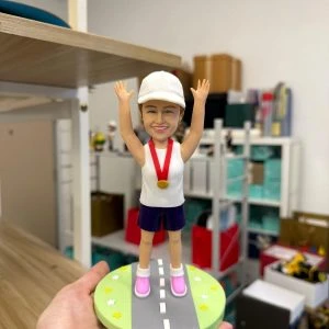 Alt: 女跑者公仔戴白帽掛金牌,雙手高舉站立於公路造型底座,馬拉松完賽紀念客製